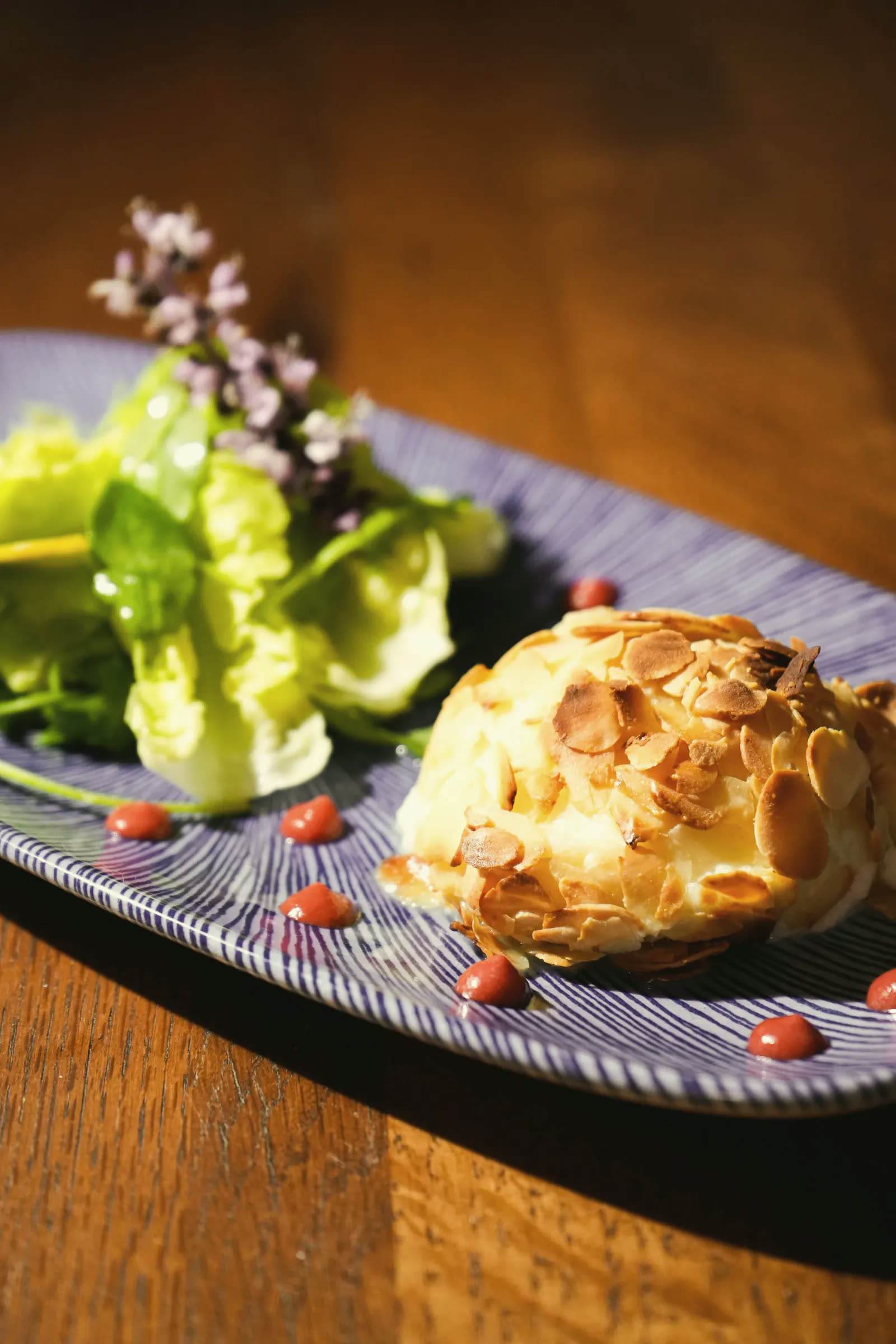 An almond-crusted crisp beside a green salad and flowers, on a blue plate