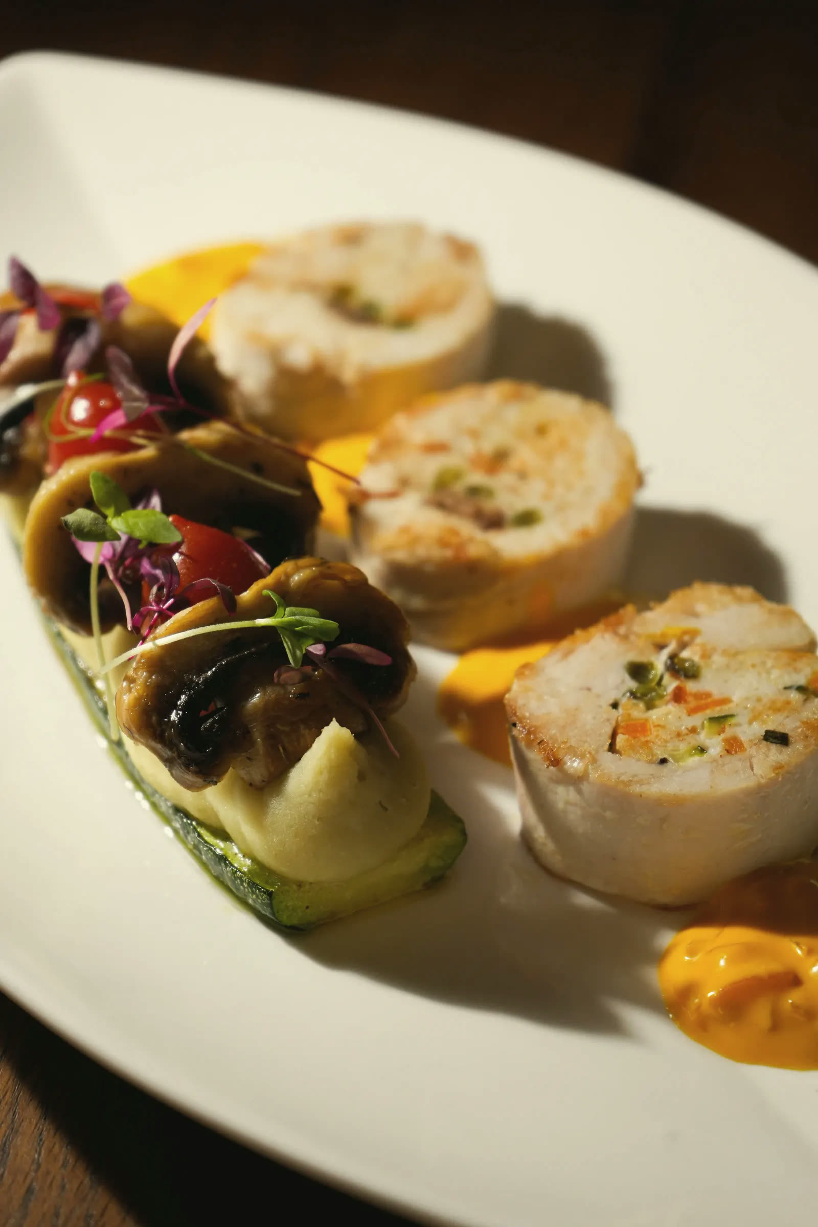 Poultry ballottines beside a stuffed courgette and two sauces