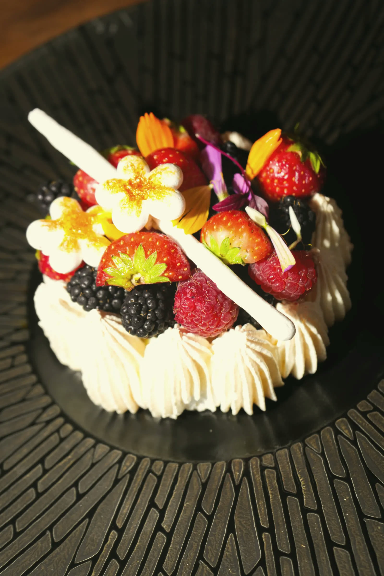 A cream gâteau crowned with red berries and frangipani flowers