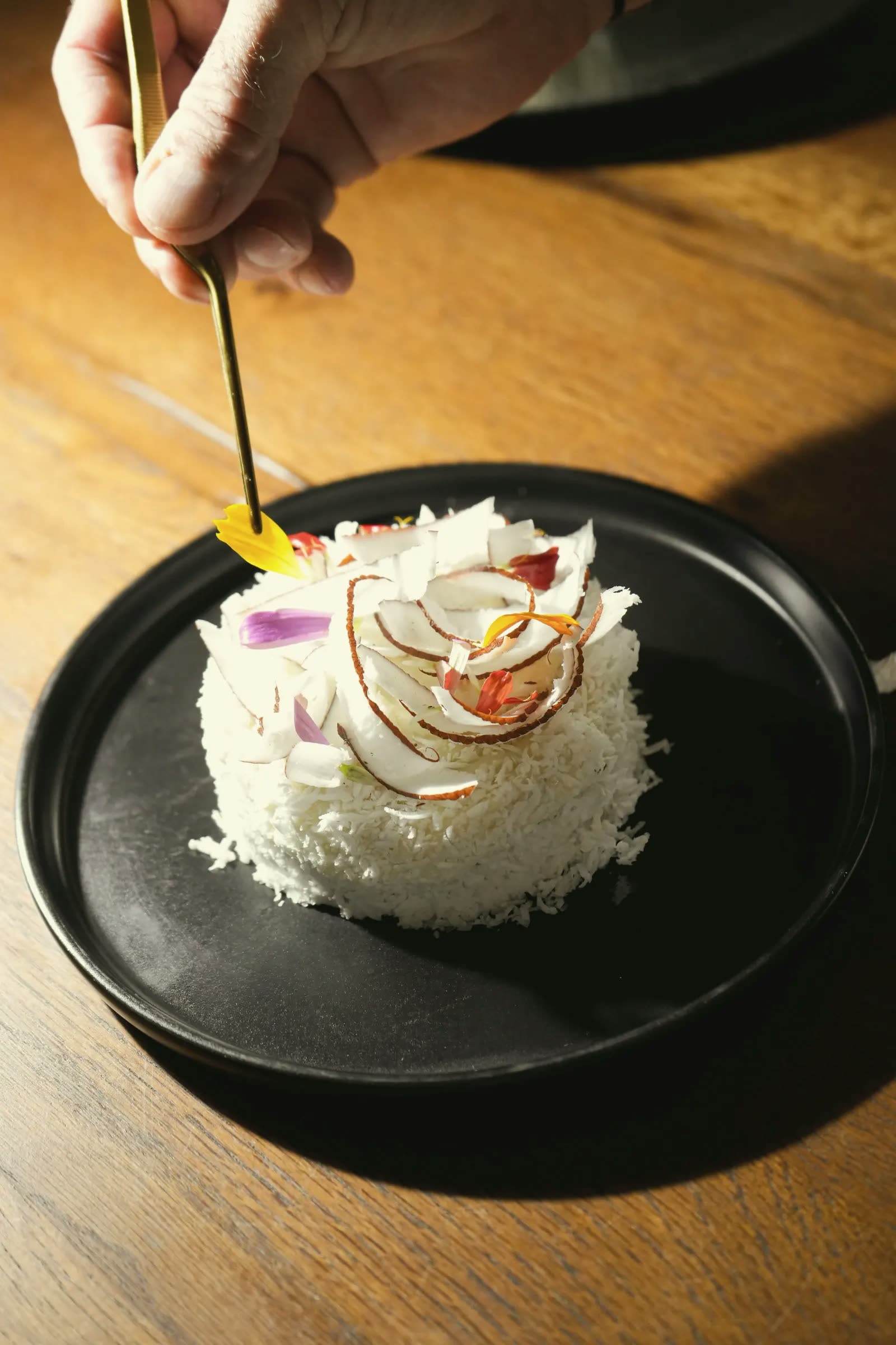 The chef finishing a coconut dome with tweezers, on a black plate