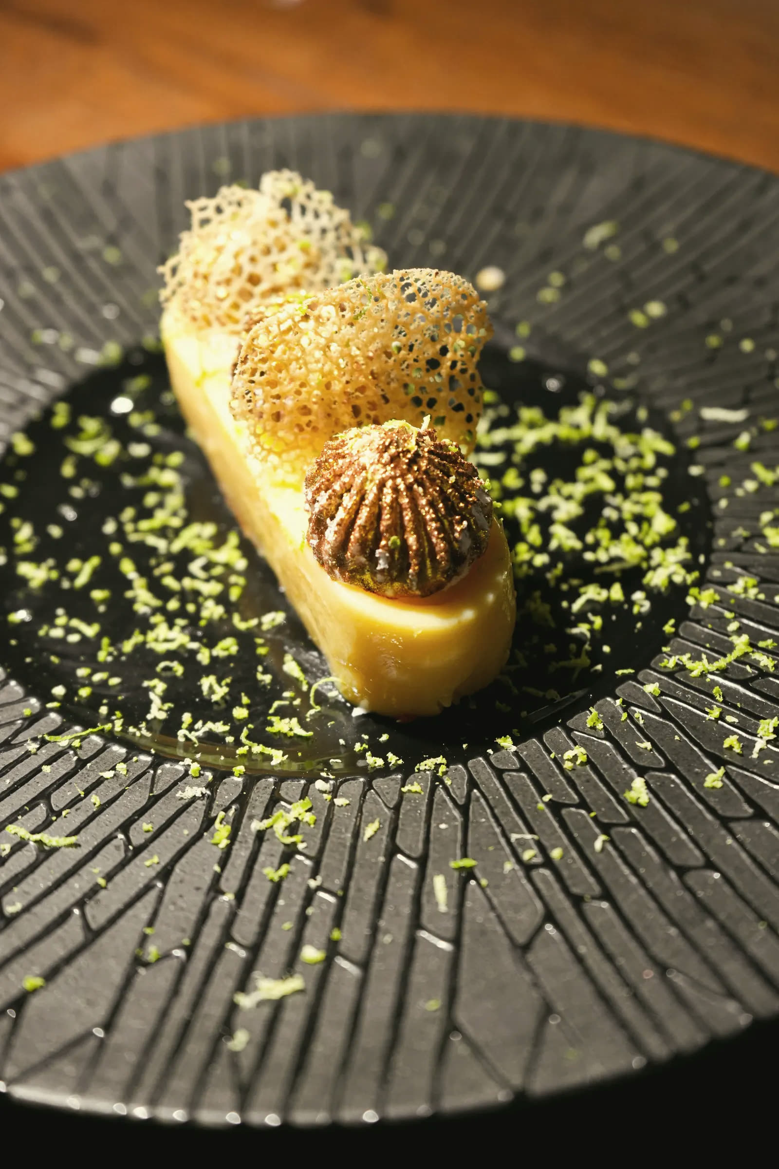 A dessert with lace tuiles and lime zest on a black plate