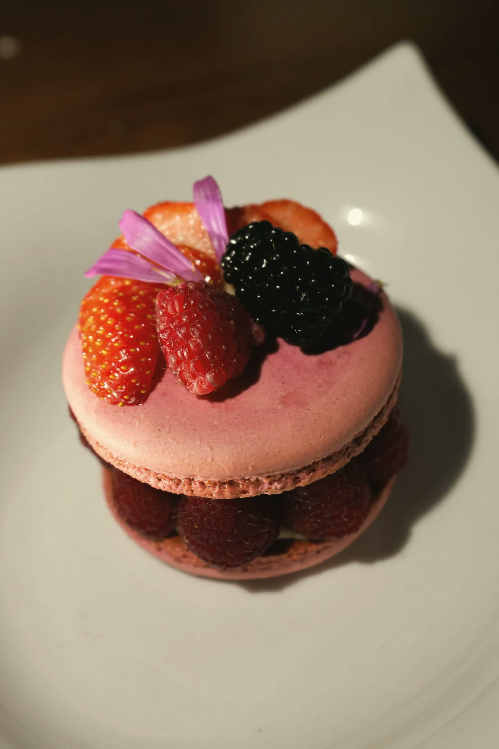 A raspberry macaron crowned with strawberries, a blackberry and petals