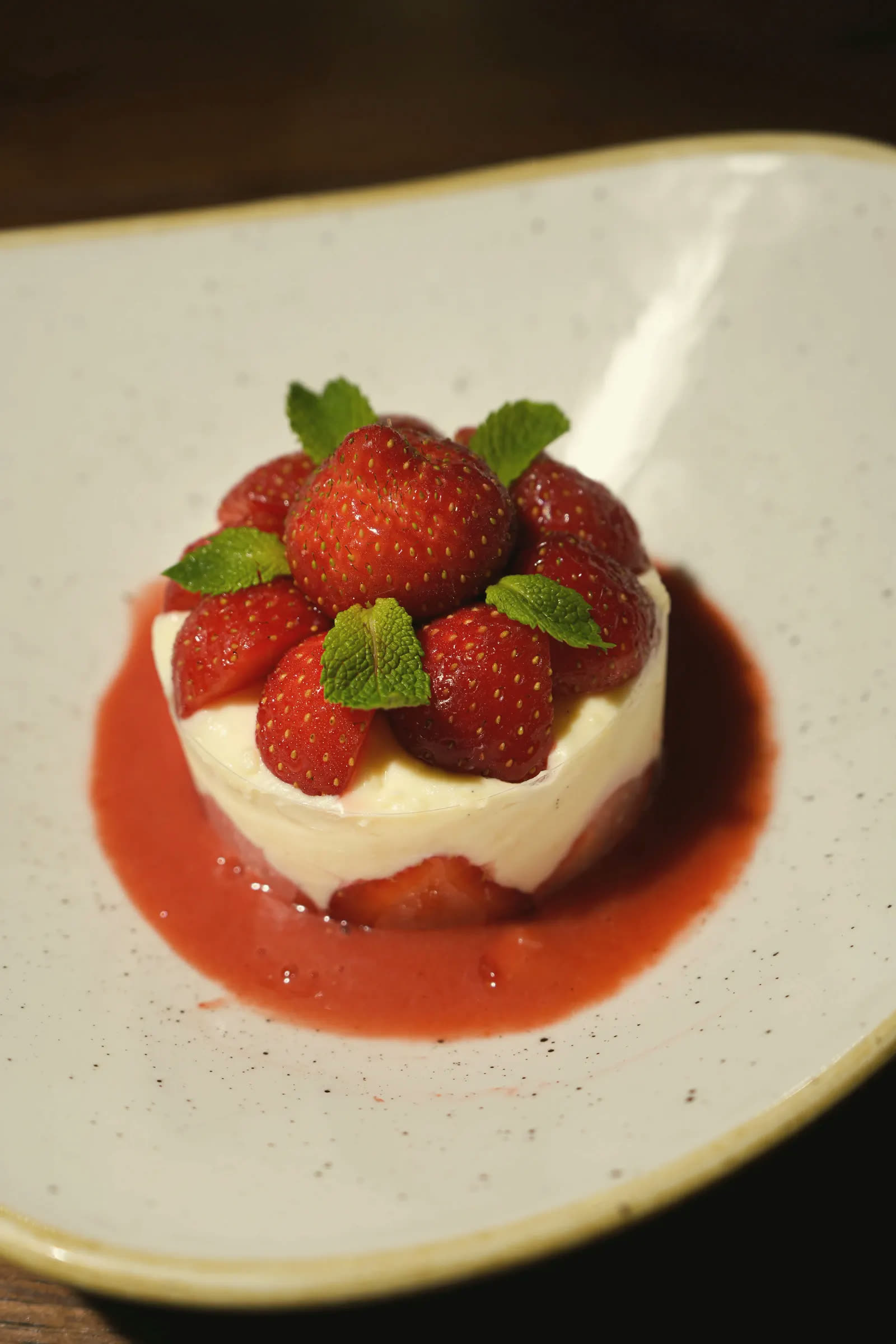 A strawberry dessert with cream, strawberry coulis and mint