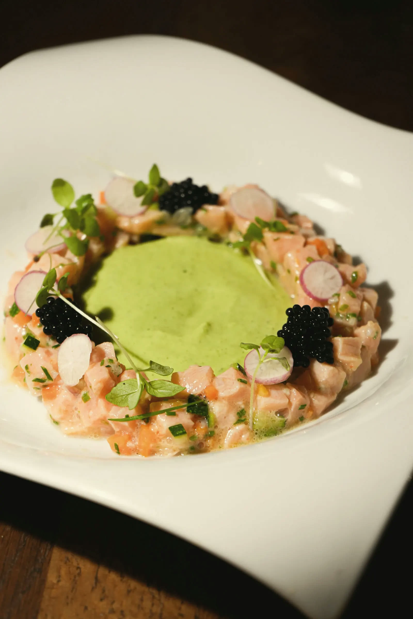 Salmon tartare set in a ring around a green mousse, with caviar and radish